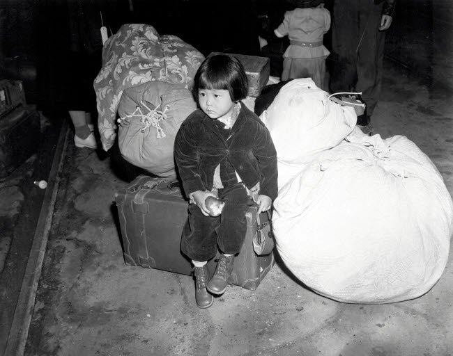 Poster print of a young evacuee of Japanese ancestry waiting for a bus with family baggage.