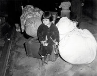 Poster print of a young evacuee of Japanese ancestry waiting for a bus with family baggage.