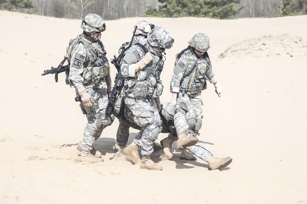 Airborne infantry paratroopers carrying injured soldier across desert sand poster print.