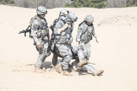 Airborne infantry paratroopers carrying injured soldier across desert sand poster print.