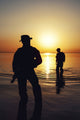 Silhouette of Army soldiers crossing a river against an orange sunset poster print by Oleg Zabielin.