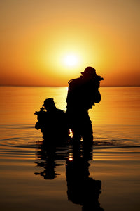 Silhouette of Army soldiers crossing a river against an orange sunset poster print by Oleg Zabielin.