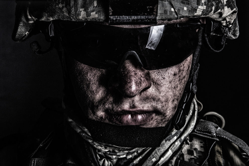 Cropped close-up portrait of a U.S. soldier in helmet and sunglasses with dirty face.