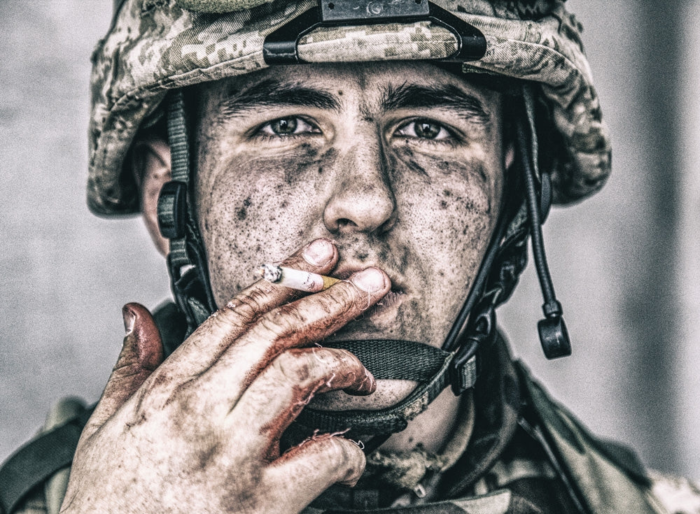 Close-up portrait of a dirty soldier smoking a cigarette with blood-stained fingers.