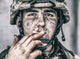 Close-up portrait of a dirty soldier smoking a cigarette with blood-stained fingers.