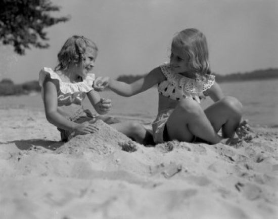 Poster print of two girls playing in sand on beach, capturing childhood joy.