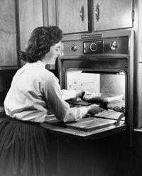 Young woman putting food into an oven poster print, perfect for kitchen decor.