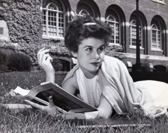 Young woman lying on the grass holding a book poster print.