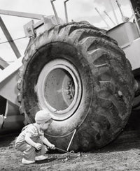Crouching boy holding a tool next to a bulldozer poster print.