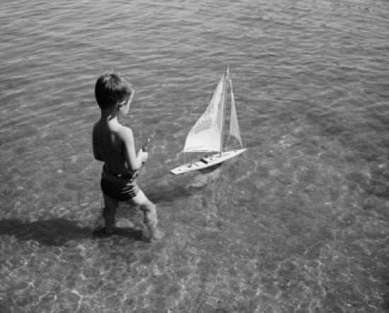 High angle view of a boy playing with a toy boat in water poster print