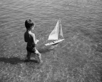 High angle view of a boy playing with a toy boat in water poster print