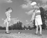 Boy playing golf with his sister poster print, capturing childhood joy.