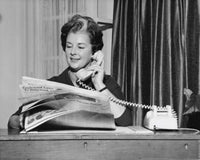 Businesswoman talking on the telephone and holding a newspaper in an office Poster Print