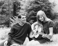 Close-up of a young woman playing guitar with a young man beside her.