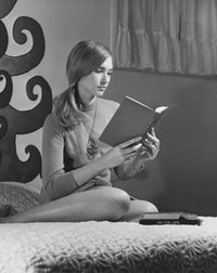 Teenage girl sitting on bed reading a book poster print