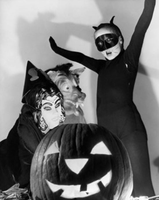 Close-up of an illuminated jack o' lantern with three people in Halloween costumes.