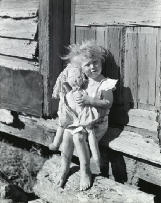 Portrait of a girl holding a doll sitting on the doorstep of a house.