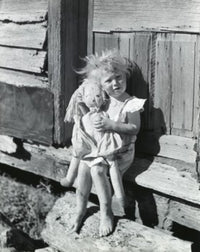 Portrait of a girl holding a doll sitting on the doorstep of a house.