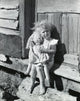 Portrait of a girl holding a doll sitting on the doorstep of a house.