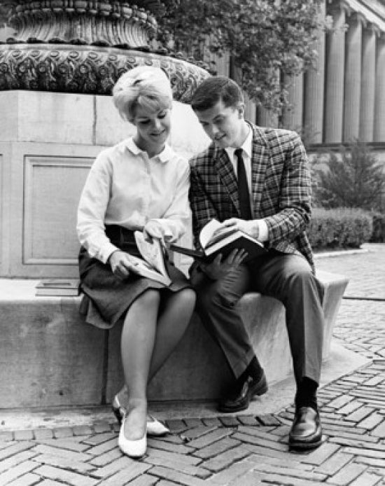 Poster print of two college students sitting on a ledge reading a book.