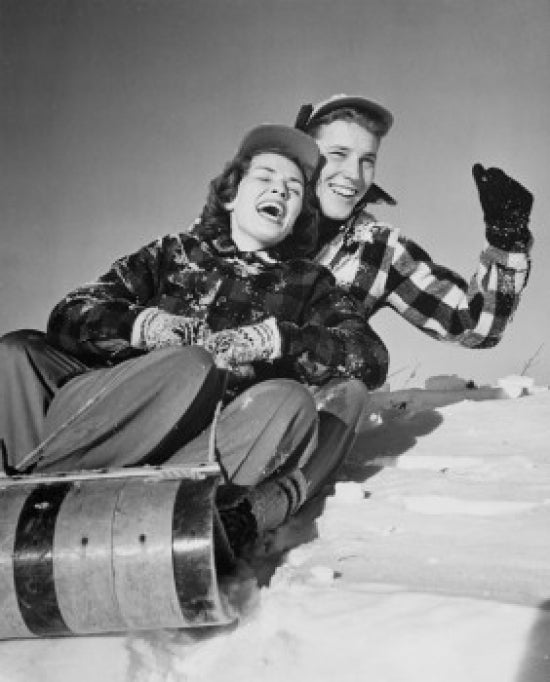 Young couple sliding on a sled in winter scenery poster print