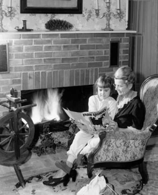 Senior woman reading a story to her granddaughter by the fireplace poster print.