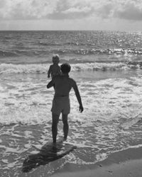 Rear view of a father carrying his son on the beach poster print.