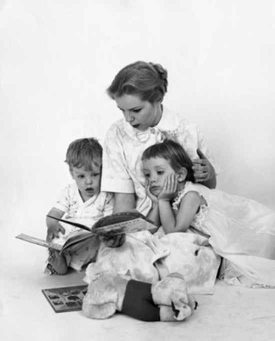 Mid adult woman reading a story book to her children poster print.