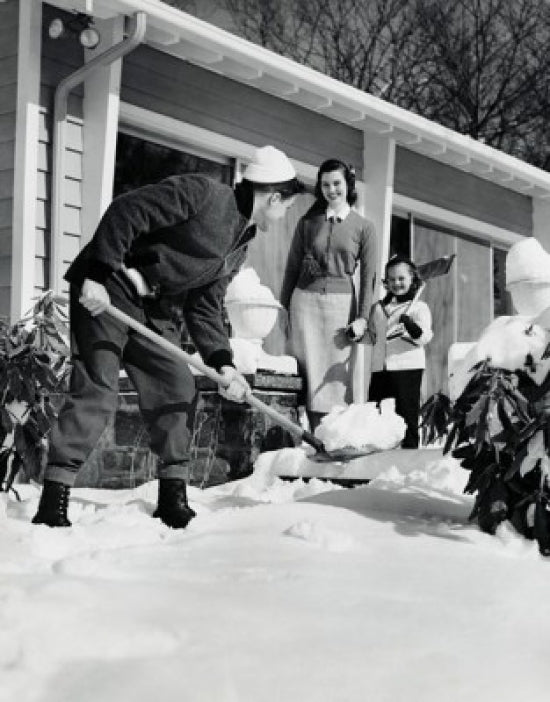 Father shoveling snow in front yard with family watching.