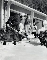 Father shoveling snow in front yard with family watching.