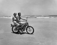 Young couple riding motorcycle on beach poster print.