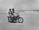 Young couple riding motorcycle on beach poster print.