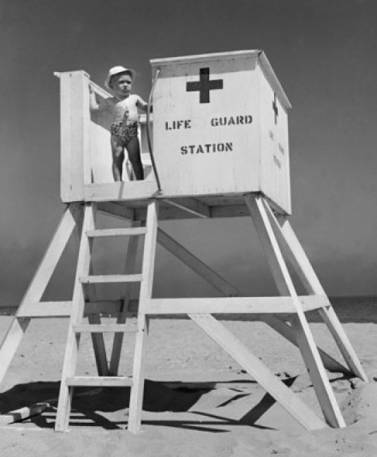 Boy standing on lifeguard station at the beach poster print