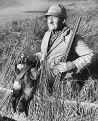 Poster print of a male hunter holding two ducks in a field.
