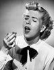 Close-up of a young woman sneezing, handkerchief in hand.
