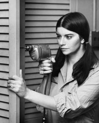 Close-up of a young woman drilling into a door poster print