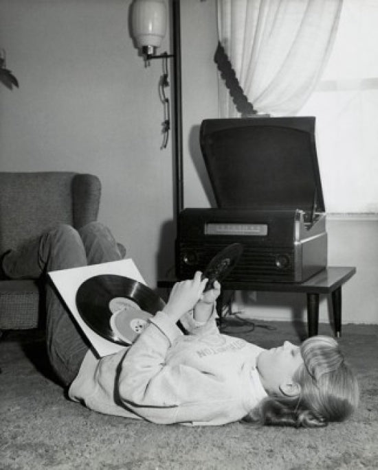 Teenage girl lying on carpet holding records poster print.