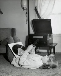 Teenage girl lying on carpet holding records poster print.