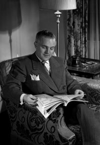 Poster print of a man sitting on a chair reading a magazine.