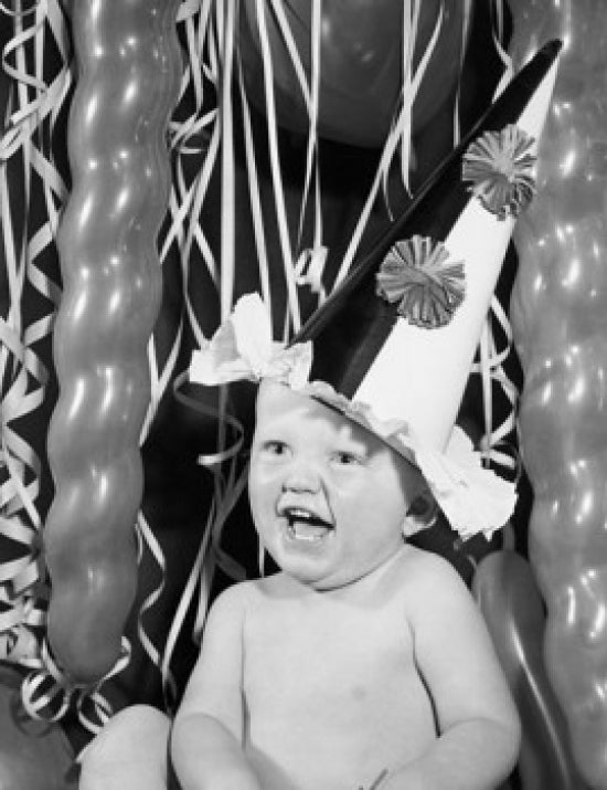 Close-up of a laughing baby boy wearing a party hat.