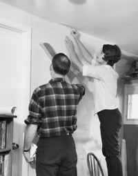 Mid adult couple applying wallpaper in a bright room poster print