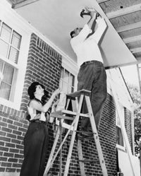 Low angle view poster print of a man and woman fixing plywood on a porch.