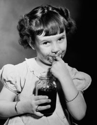 Portrait of a girl holding a jar of jam and licking her finger.