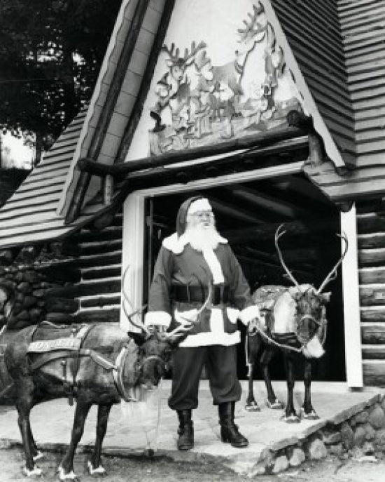 Santa Claus standing with two reindeer in front of a building poster print