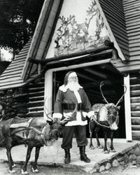 Santa Claus standing with two reindeer in front of a building poster print