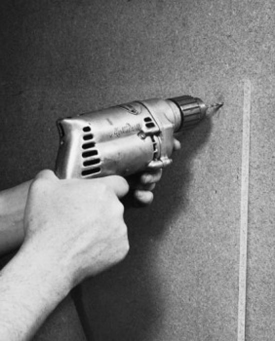 Close-up image of a person's hands drilling into a wall.