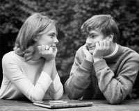 Close-up poster print of a teenage couple sitting at a table looking at each other.