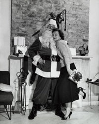 Poster print of a young woman holding a Christmas present and hugging Santa Claus in front of a fireplace.