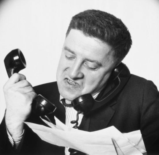 Close-up poster print of a frustrated businessman using two telephones.