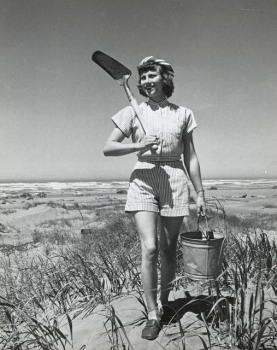 Young woman walking on Long Beach carrying sand pail and shovel poster print.